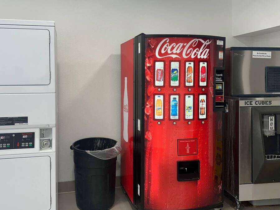 Una máquina expendedora con opciones de Coca-Cola y Sprite, un bote de basura y un dispensador de hielo.