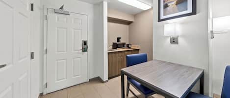 Habitación de hotel con mesa de comedor, sillas, microondas y cafetera.
