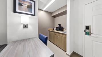 Habitación de hotel con mesa de comedor, una silla azul, kitchenette y puerta con cerradura electrónica.