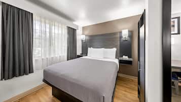 A hotel room with a large bed, a bedside table with a lamp, a wall-mounted phone, and a window with curtains.
