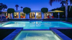 Uma casa moderna com piscina, duas janelas grandes e um espaço de pátio com mobiliário para exterior.