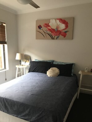 Relax in a serene bedroom with a large bed, artwork, and a window with blinds.