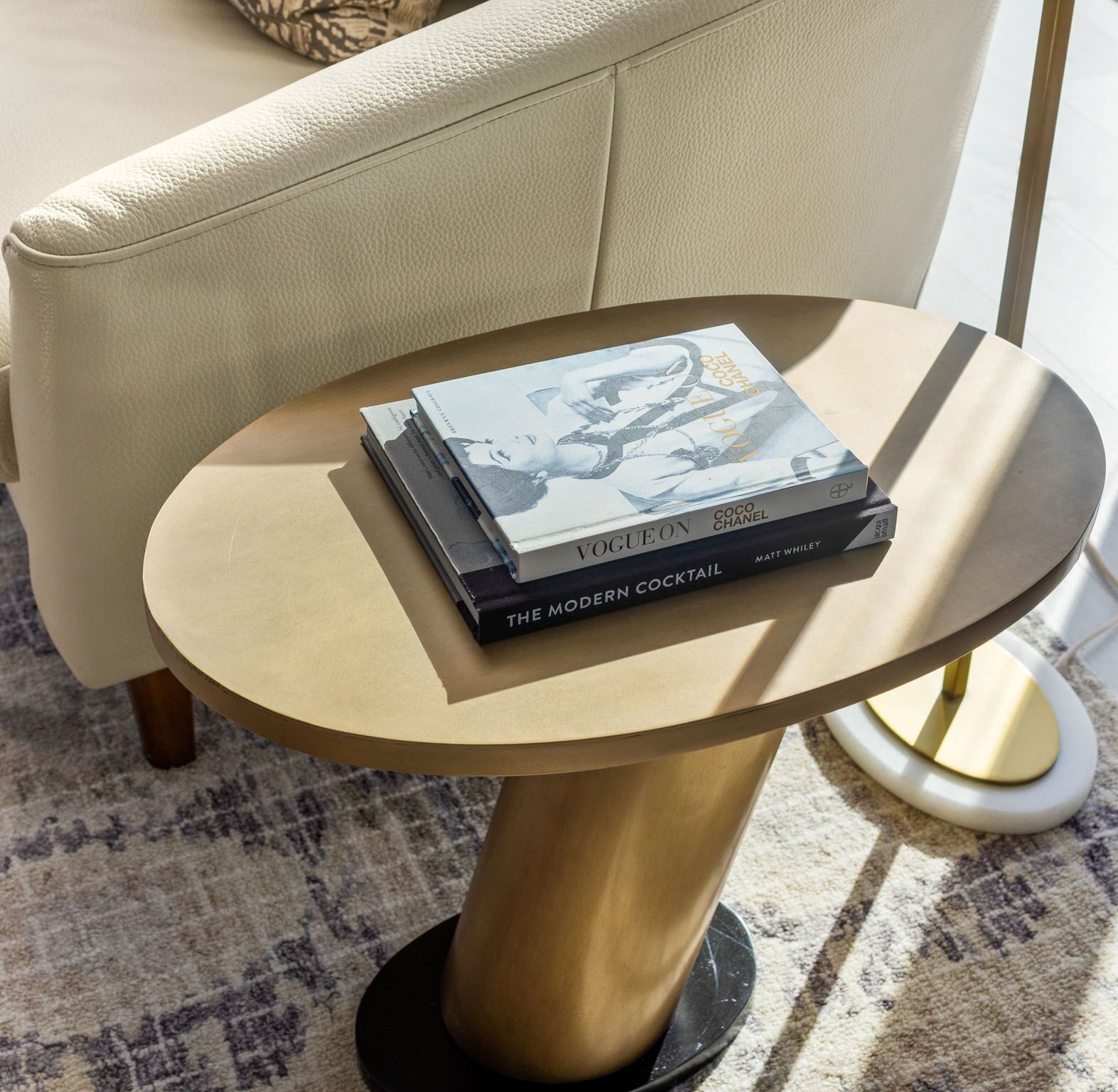 Une table ronde sur laquelle est posée une pile de livres, dont « Vogue sur Coco Chanel » et « Le cocktail moderne ».