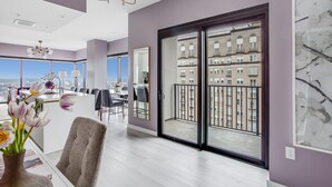 Ein modernes Wohnzimmer mit großem Fenster, einem Essbereich und Blick auf ein gegenüberliegendes Gebäude.