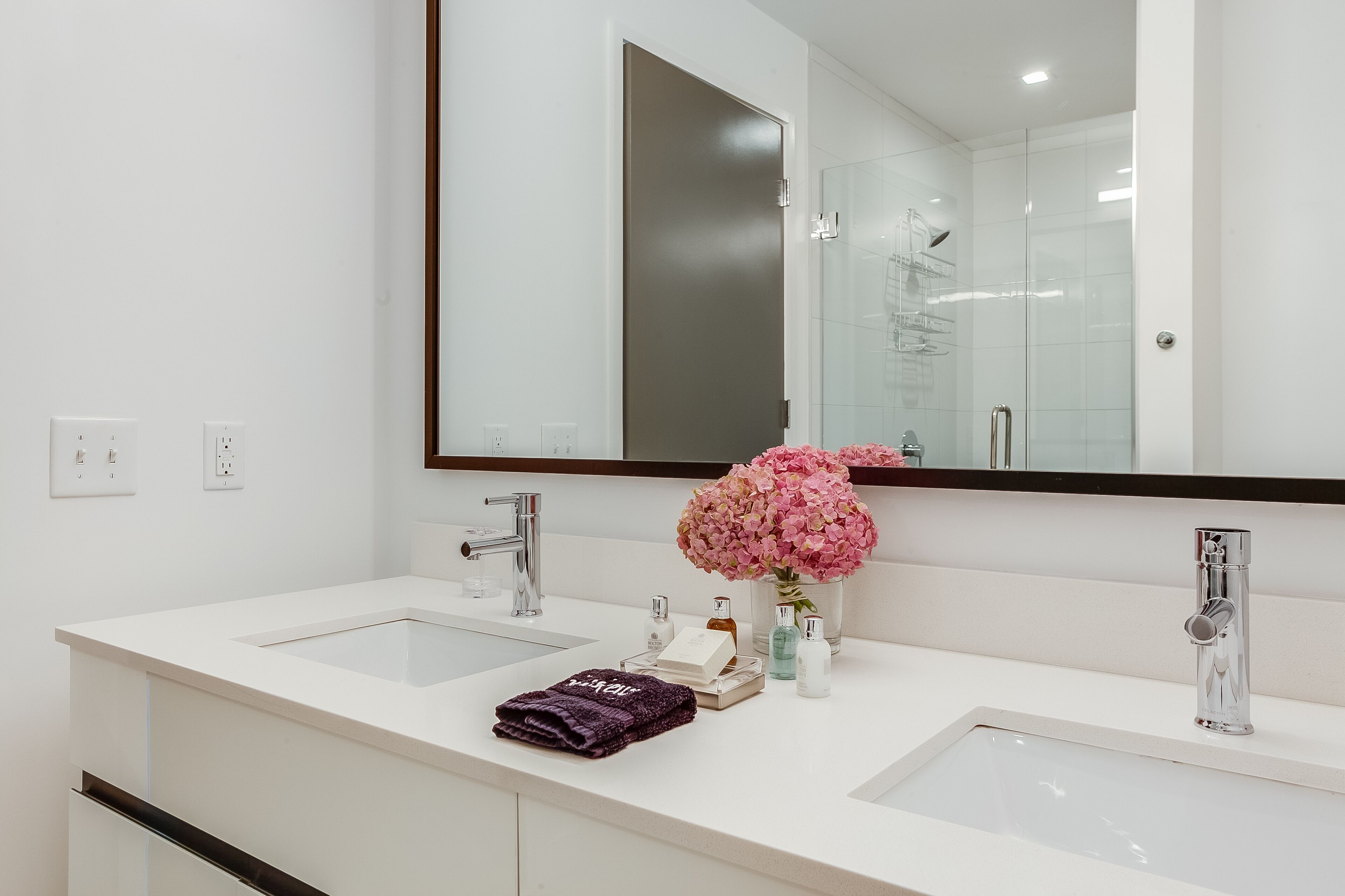 Une salle de bain moderne avec deux lavabos, un grand miroir et une douche à l’italienne.