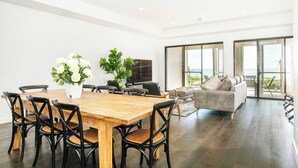 Una sala moderna con una mesa de comedor de madera, sillas negras, un sofá gris y un televisor grande.