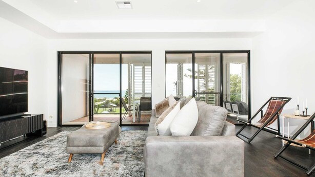 Una sala de estar moderna con un sofá gris, una mesa de centro y un televisor. Hay un ventanal con vistas al exterior.