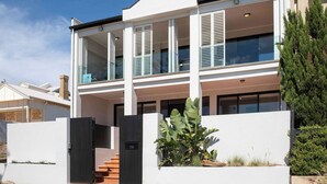 Una casa moderna de dos pisos con balcón, entrada con portón y jardín cuidado.