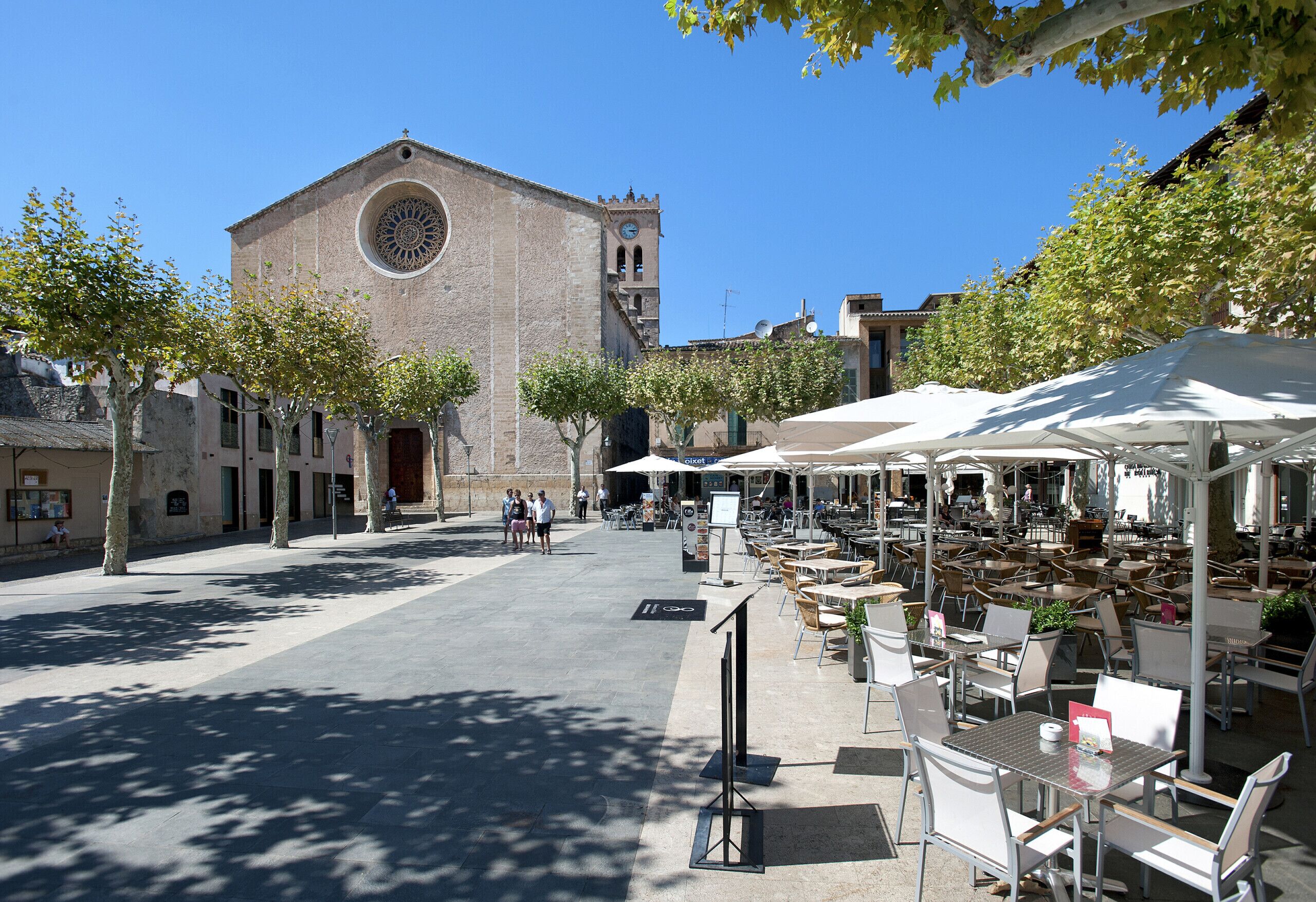 A courtyard with outdoor seating, a historic building with a clock tower, and trees providing shade.