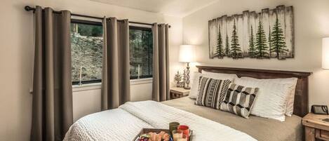 Habitación de hotel con cama, bandeja de desayuno, un cuadro de árboles y una ventana con cortinas.
