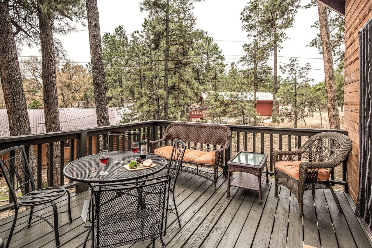 A wooden deck with wicker furniture, a table with a bottle of wine, and a glass.