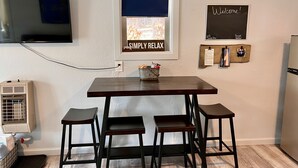 A compact kitchen with a dark wooden table and four stools, a window with a view, a mounted TV, and a 'Welcome!' sign. - Simply Relax in the Mountains! (Cloudcroft)