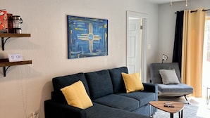 A modern living room with a dark grey sectional sofa, a small wooden coffee table, and a grey armchair. There is a ceiling fan, a blue abstract painting, and a door with a white frame. - Simply Relax in the Mountains! (Cloudcroft)