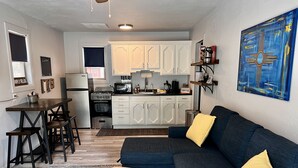 A compact living space with a kitchenette, a sofa with yellow cushions, a coffee table, and a painting on the wall. - Simply Relax in the Mountains! (Cloudcroft)