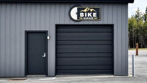 Un edificio con un letrero que dice 'BIKE GARAGE', una puerta de garaje cerrada y una pequeña puerta a la izquierda.