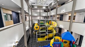Zona de juegos infantiles con toboganes y estructuras para escalar, ubicada en un pasillo de hotel con varios pisos y diseño moderno.