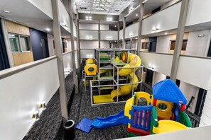 Ein Spielbereich für Kinder mit Rutschen und Klettergerüsten, gelegen in einem Hotelkorridor mit mehreren Etagen und modernem Design.