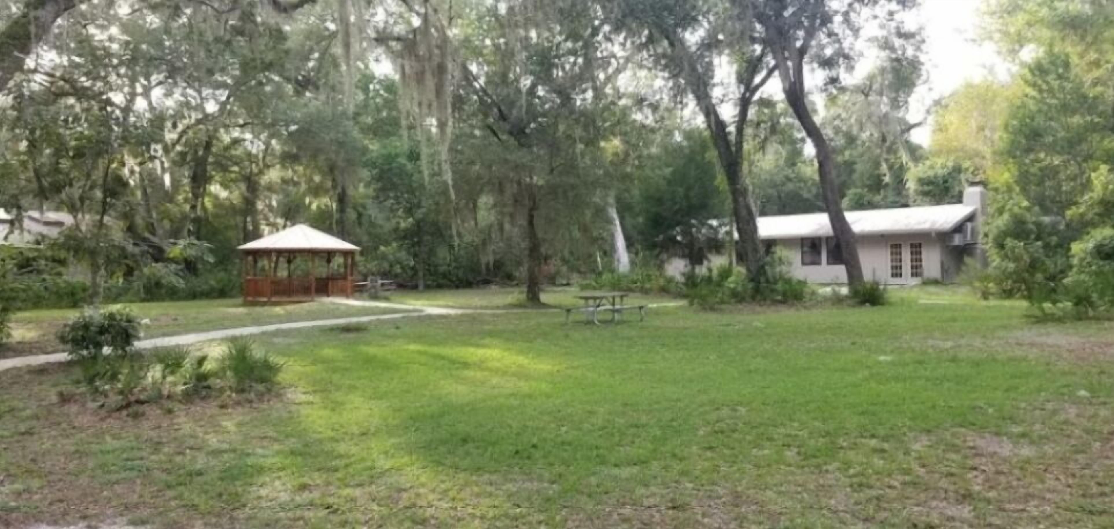 A gazebo, picnic table, and a building surrounded by trees in a grassy area.