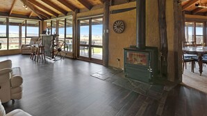 A spacious living area with a large fireplace, wooden beams, and large windows offering a view of the outdoors.
