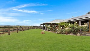 A grassy area with a wooden fence, a covered structure with a roof, and a garden with various plants and flowers.