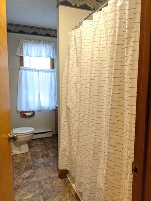 A bathroom with a toilet, a shower curtain, and a window with a curtain. - Fun For the Whole Crew! (Davis)