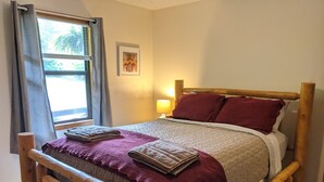 Un lit en bois avec une tête de lit, une fenêtre avec des rideaux, une lampe de chevet et un tableau encadré au mur.
