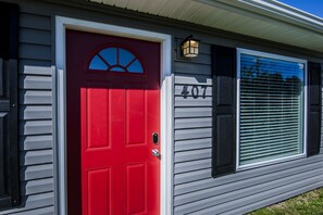 Welcome to a charming home with a distinctive red front door and a cozy white-framed window.