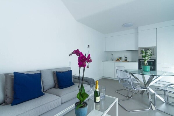Una sala de estar moderna con un sofá, una mesita de centro de vidrio y un jarrón con flores.