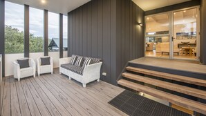 Eine moderne Außenterrasse mit Korbmöbeln, einer Holztreppe und Blick ins Innere.