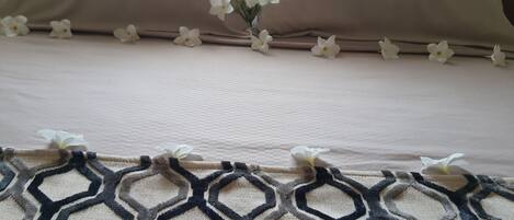 A bed with a beige bedspread and a geometric patterned rug.