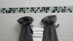 A bathroom with a towel rack holding two dark towels and a stack of white towels.