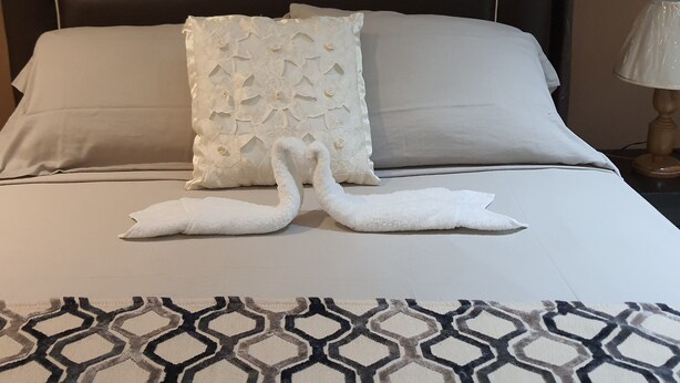 A bed with a geometric patterned bedspread, two pillows, and two swan-shaped towels on the bed.