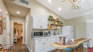 A compact kitchen with white cabinets, a microwave, an oven, and a refrigerator. There is a wooden table with chairs and a hanging light fixture above. - POOL OASIS! Super Reviews! EV Charger/1BR King/Wash/Dryer/Kitchenette/Sleeps 4 (Gilbert)