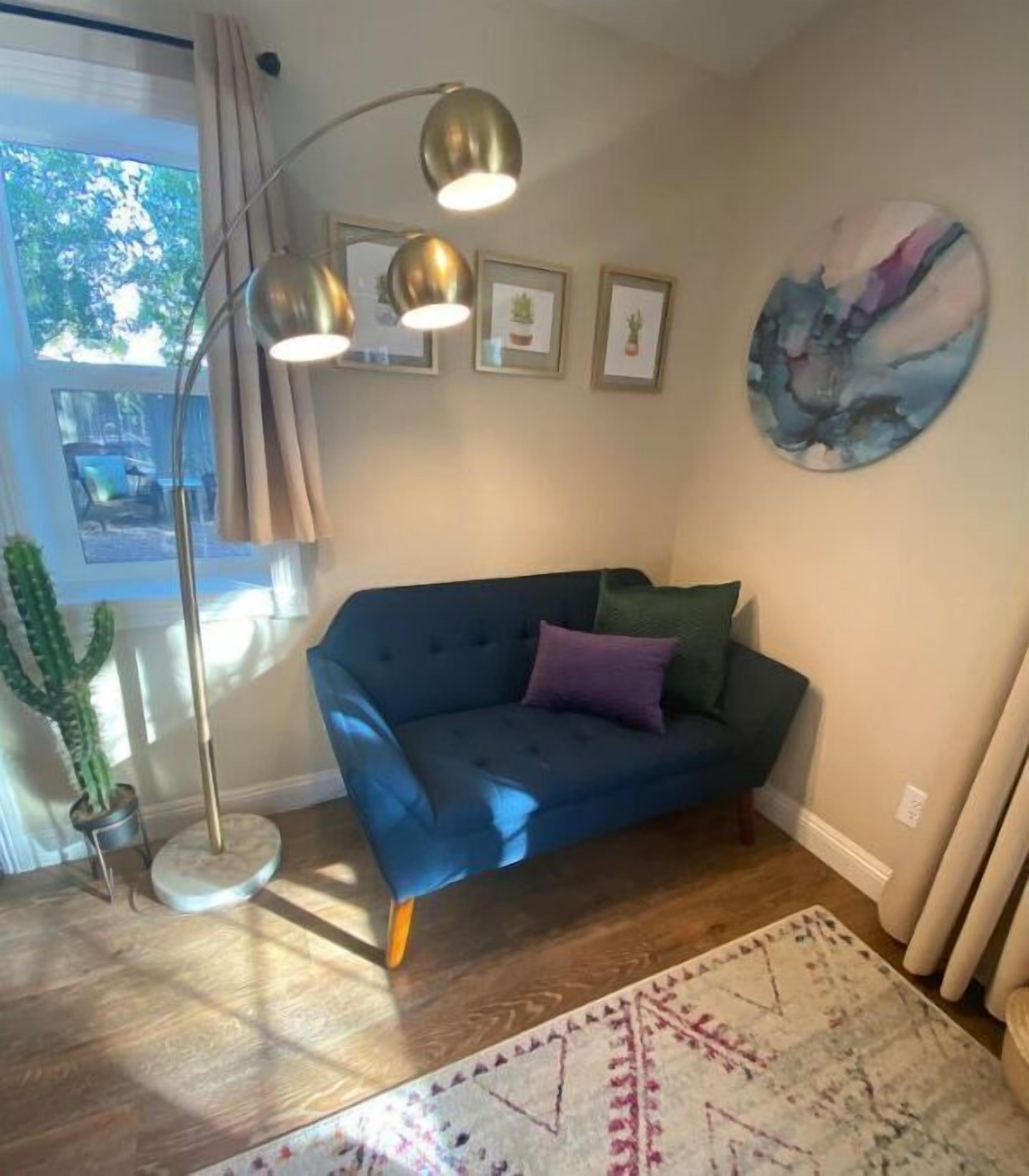 A living room with a blue sofa, a floor lamp, a cactus, and a painting on the wall.