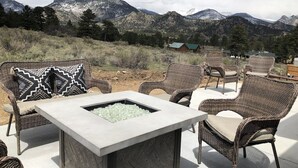 An outdoor seating area with wicker chairs and a stone table, overlooking a mountainous landscape.