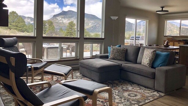 A spacious living room with a gray sectional sofa, two lounge chairs, and a large window offering a mountain view.