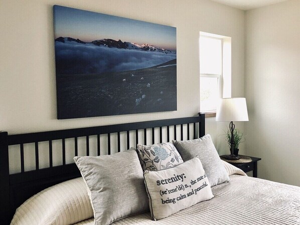 Une chambre à coucher avec un lit, des oreillers, une table de chevet, une lampe et un tableau accroché au mur.