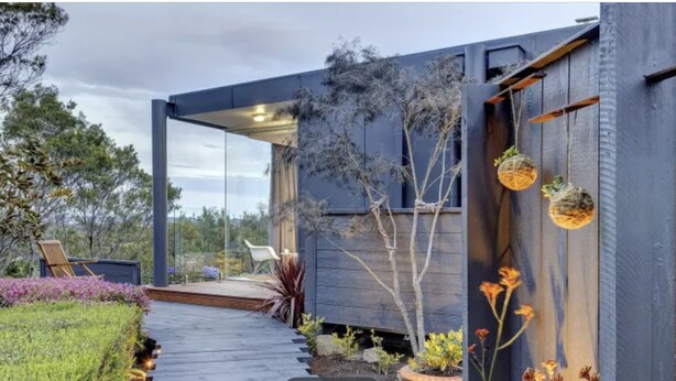 A modern house with a glass door entrance, a wooden deck, and outdoor seating.