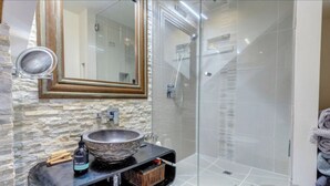 A bathroom with a stone sink, a mirror, and a glass shower enclosure.