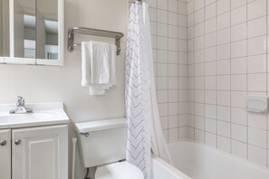 Bathroom features a white sink, toilet, and bathtub, with a herringbone-patterned shower curtain and large, square tiles on the walls.