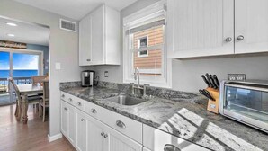 A kitchen with white cabinets, a granite countertop, a stainless steel sink, and a toaster. - Sunset Bay LBI lower unit (Long Beach)