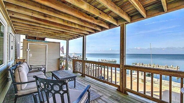 A covered outdoor area with a wooden deck, a table, and chairs. - Sunset Bay LBI lower unit (Long Beach)