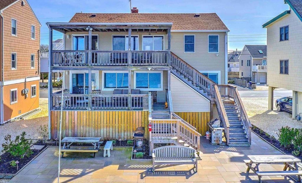 Ein zweistöckiges Haus mit Balkon, einer Treppe und einer Terrasse mit Bänken.