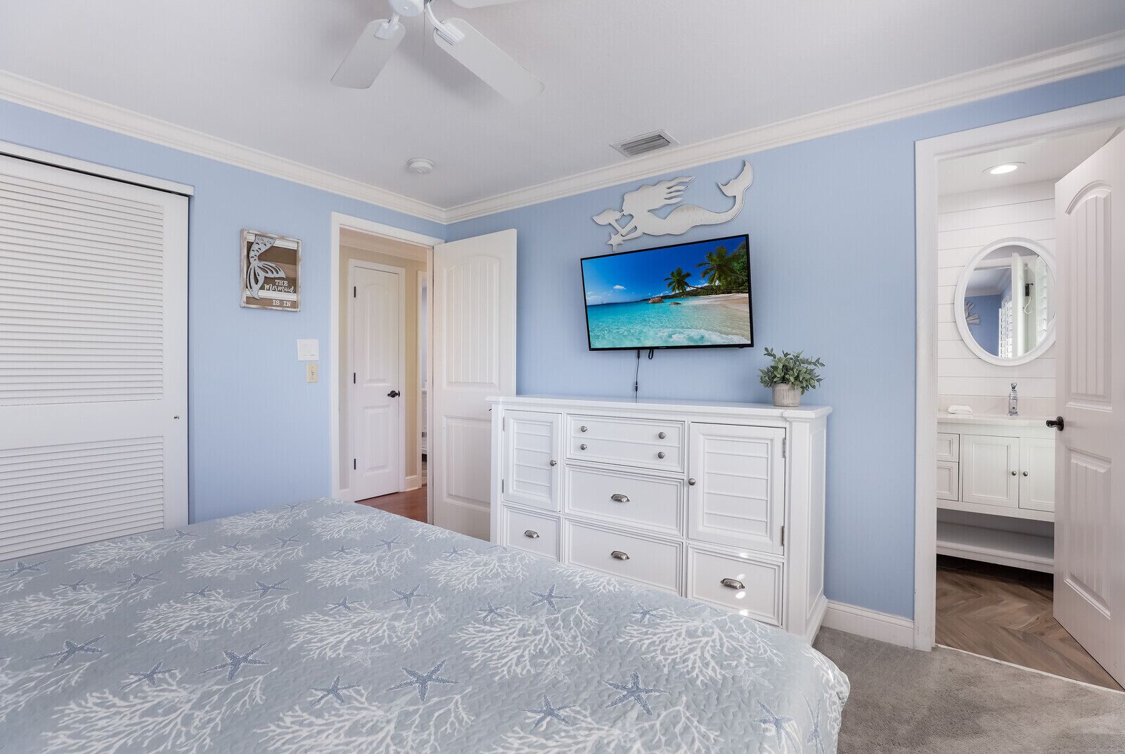 Quarto com cama, penteadeira, televisão e porta que dá para outro cômodo.