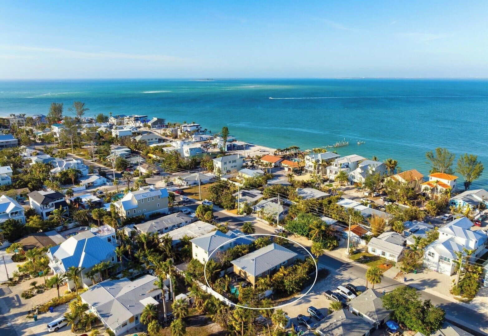 An aerial view of a coastal residential area with houses, roads, and a clear view of the ocean.