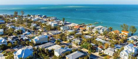 An aerial view of a coastal residential area with houses, roads, and a clear view of the ocean.