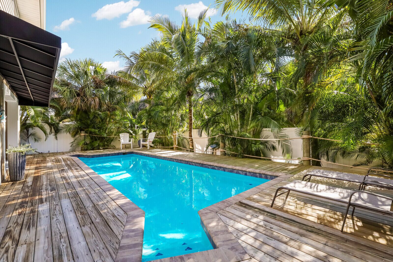 A swimming pool surrounded by wooden decking, with white chairs and a rope barrier.