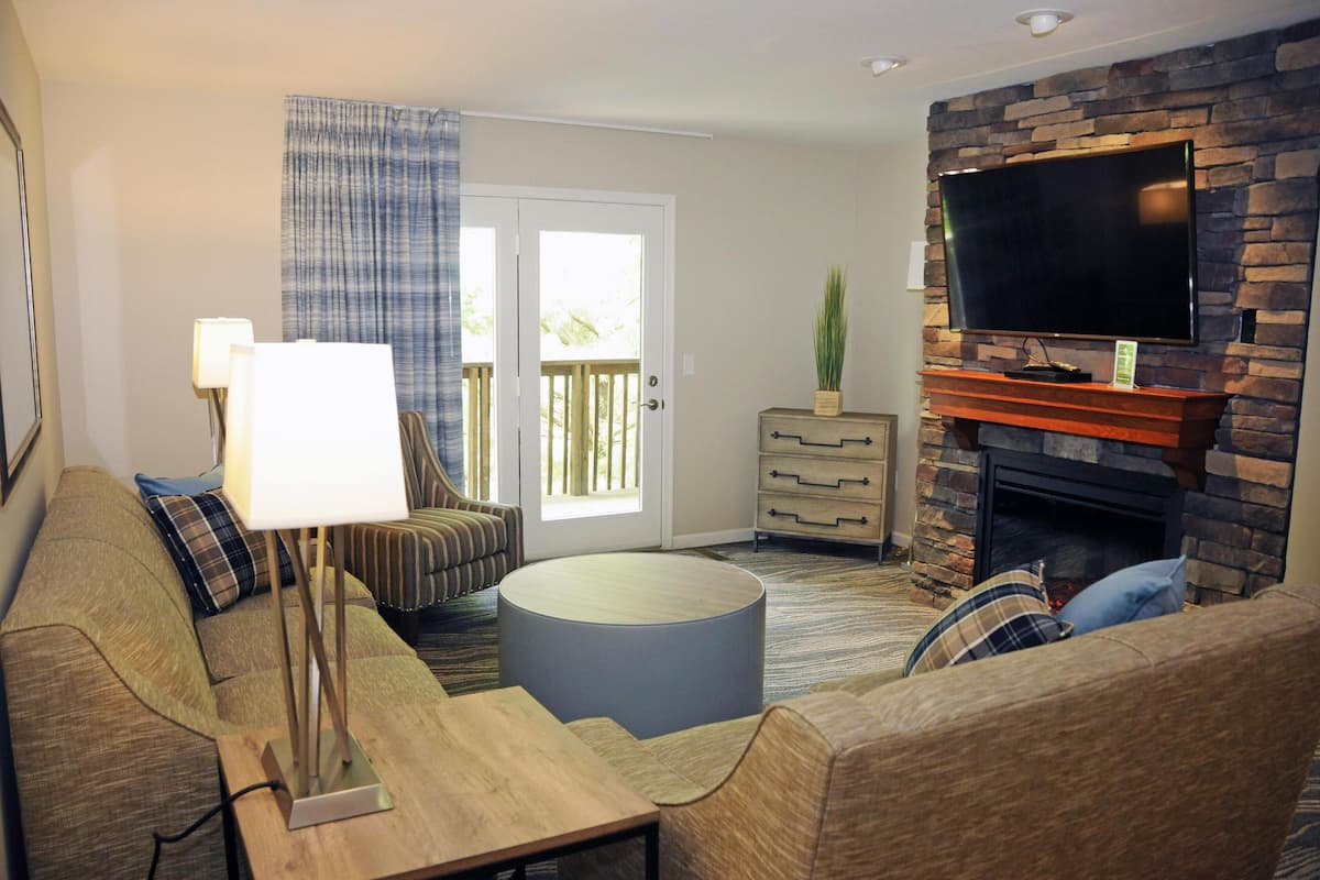 A living room with a sofa, a round coffee table, a lamp, a TV, a fireplace, and a door leading to a balcony.