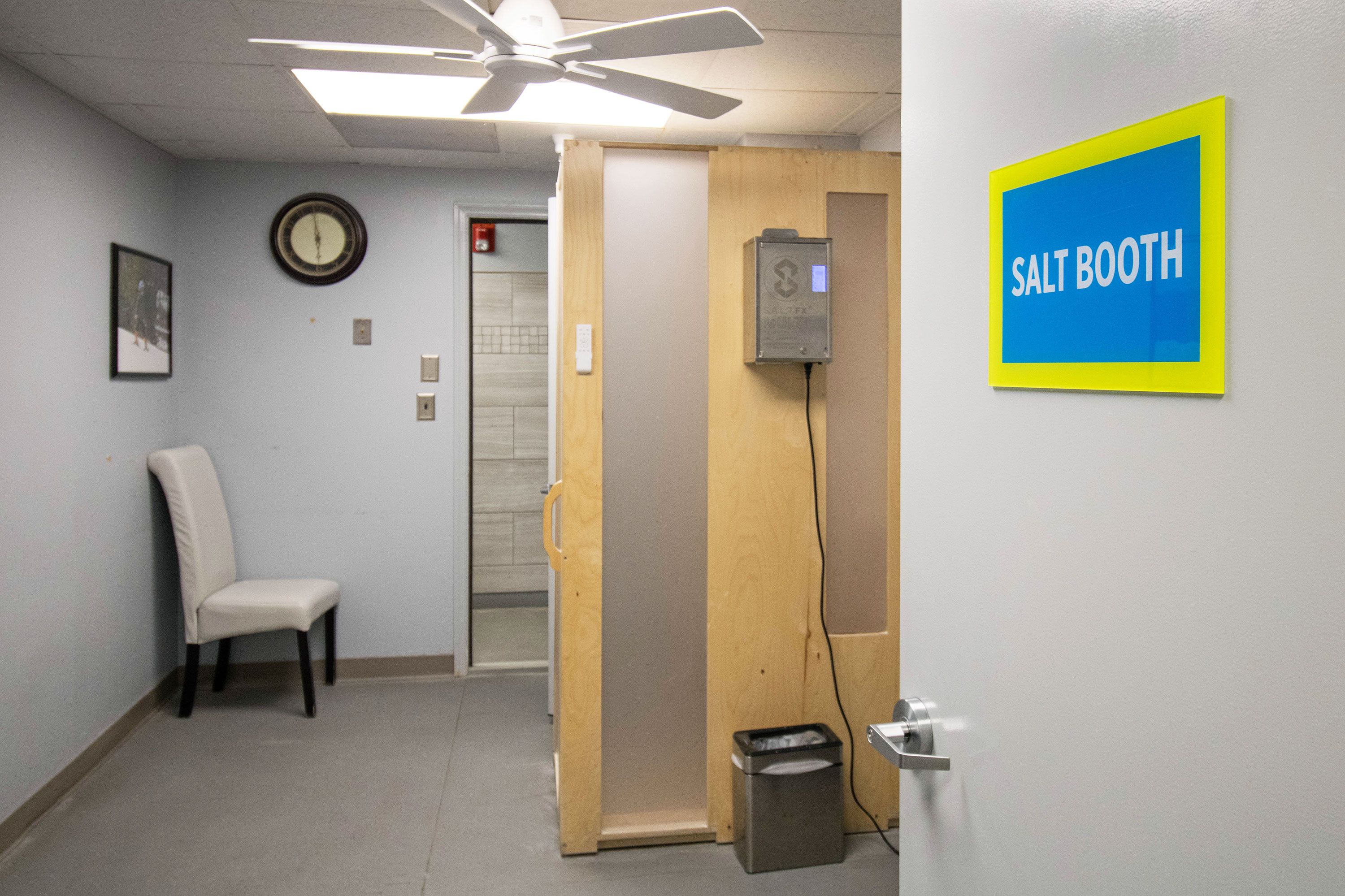 A hallway with a chair, a clock, a salt booth sign, and an elevator.