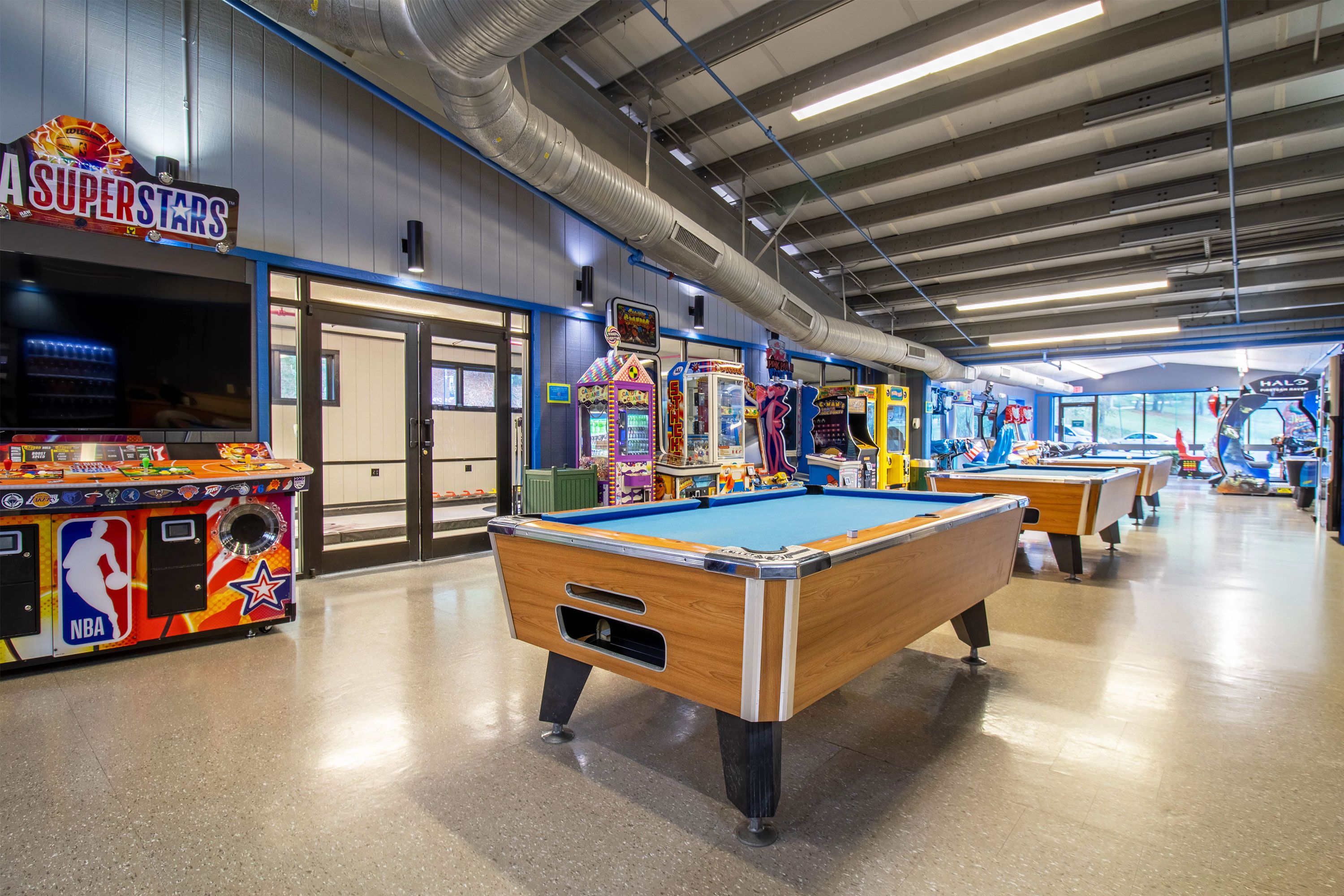 An indoor recreational area with pool tables, arcade games, and a basketball-themed game machine.